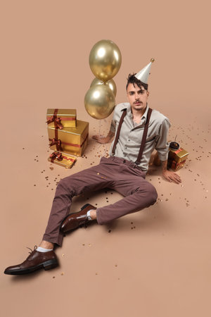 Cool young man with gifts celebrating Birthday on beige background