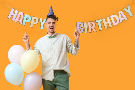 Happy young man with balloons celebrating on yellow backgroundの写真素材