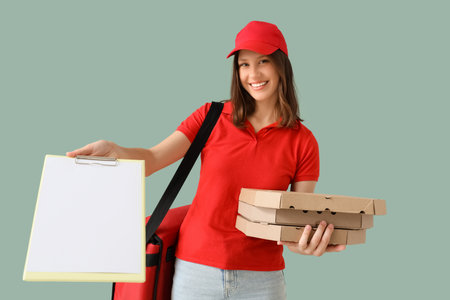 Female courier with pizza boxes and blank clipboard on green backgroundの写真素材