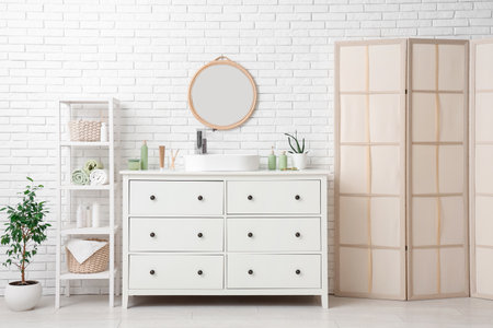 Interior of light bathroom with mirror, sink and toiletry on chest of drawersの写真素材