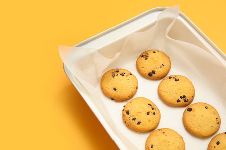 Baking tray with tasty cookies on yellow background, closeup