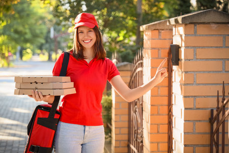 Female courier with pizza boxes ringing bell at gate of houseの写真素材