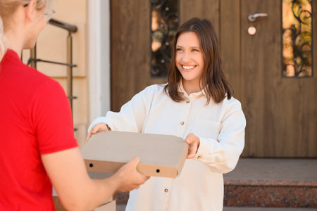 Young woman receiving pizza from courier outdoorsの写真素材