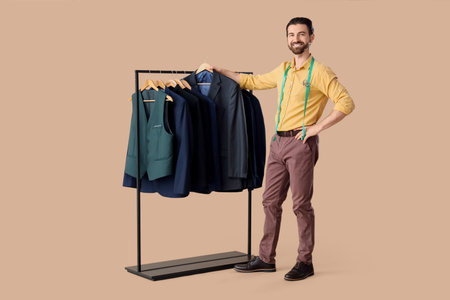 Male tailor and rack with jackets on beige background