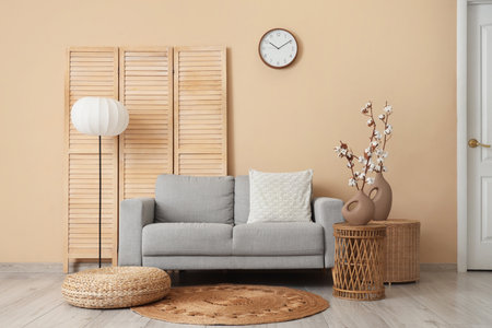 Gray sofa, pouf, wicker tables and vases with cotton flowers in interior of living roomの写真素材