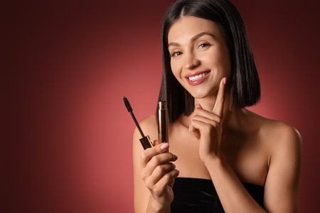 Beautiful young woman with mascara on dark red background, closeupの写真素材