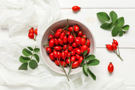 Bowl with fresh rose hip berries and leaves on white wooden backgroundの写真素材