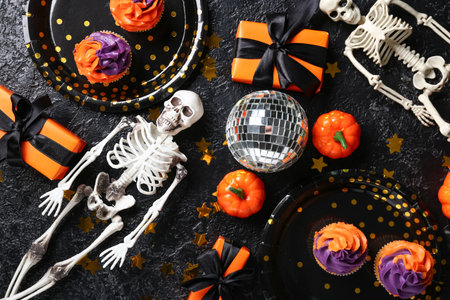Tasty cupcakes with disco ball, gift boxes, skeletons and Halloween decor on black grunge backgroundの写真素材
