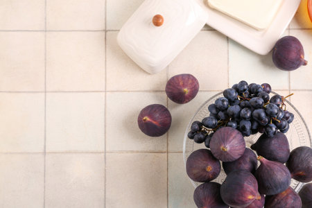 Bowl with fresh ripe figs and grape on beige tile background, closeupの写真素材