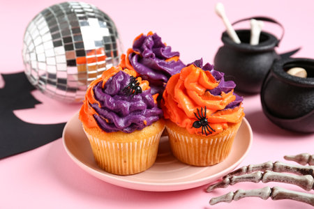 Disco ball with tasty cupcakes, skeleton hand and Halloween decor on pink backgroundの写真素材