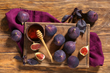 Board with fresh ripe figs, red basil leaves and bowl of honey on wooden backgroundの写真素材