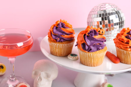Glass of tasty cocktail with cupcakes, disco ball and Halloween decor on color backgroundの写真素材