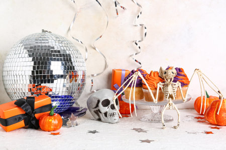 Tasty cupcakes with disco ball, gift boxes, bat skeleton and Halloween decor on white backgroundの写真素材