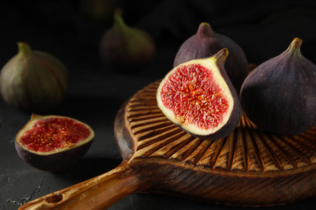 Wooden board with fresh ripe figs on black background, closeupの写真素材