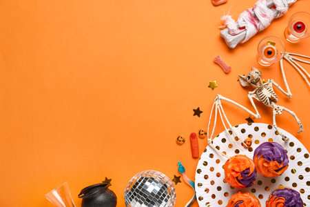 Tasty cupcakes with disco ball, shot glasses, bat skeleton and Halloween decor on orange backgroundの写真素材