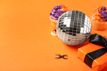 Disco ball with cupcakes, gift box and Halloween decor on orange backgroundの写真素材