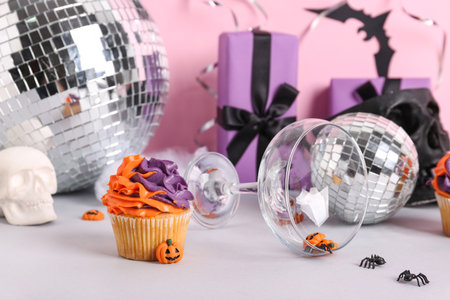 Tasty cupcake with disco balls, skulls, gift boxes, glass and Halloween decor on color backgroundの写真素材