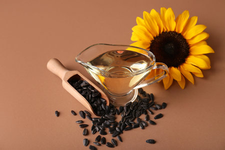 Gravy boat of oil with sunflower, scoop and seeds on brown backgroundの写真素材