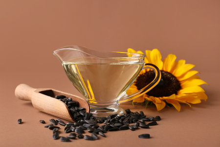 Gravy boat of oil with sunflower, scoop and seeds on brown backgroundの写真素材