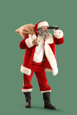 Santa Claus with bag full of gifts looking through binoculars on green backgroundの写真素材