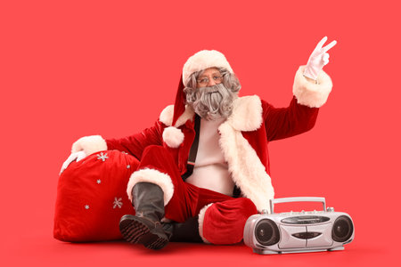 Santa Claus with bag full of gifts and boombox sitting on red backgroundの写真素材