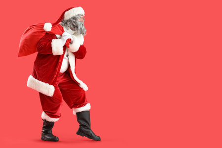 Santa Claus with bag full of gifts sneaking on red backgroundの写真素材