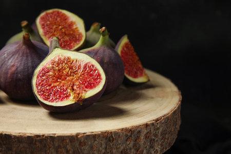 Wooden board with fresh ripe figs on black background