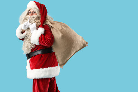 Santa Claus with bag full of gifts showing silence gesture on blue backgroundの写真素材