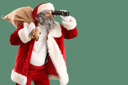 Santa Claus with bag full of gifts looking through binoculars on green backgroundの写真素材