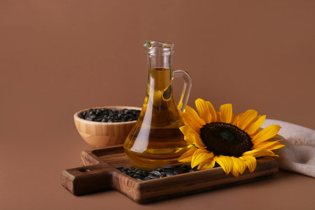 Jug of oil, sunflower and bowl with seeds on brown backgroundの写真素材