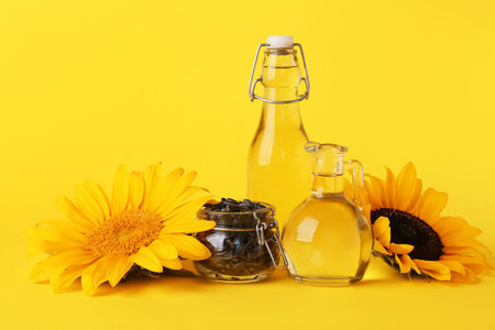 Sunflowers, seeds, bottle and jug of oil on yellow backgroundの写真素材