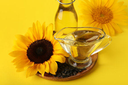 Sunflowers with seeds, bottle and gravy boat of oil on yellow backgroundの写真素材