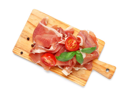 Wooden board with delicious prosciutto slices, basil leaves, peppercorns and cherry tomato on white backgroundの写真素材