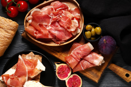 Plate with delicious prosciutto slices, figs and olives on black wooden backgroundの写真素材