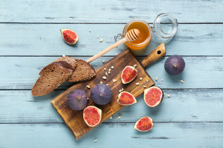 Composition with cutting board, fresh ripe figs, toasts and jar of honey on blue wooden backgroundの写真素材