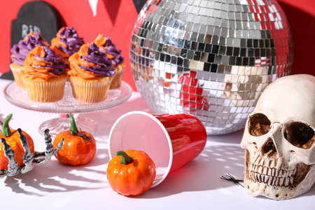Tasty cupcakes with disco ball, skull, plastic cup, skeleton hand and Halloween decor on color backgroundの写真素材