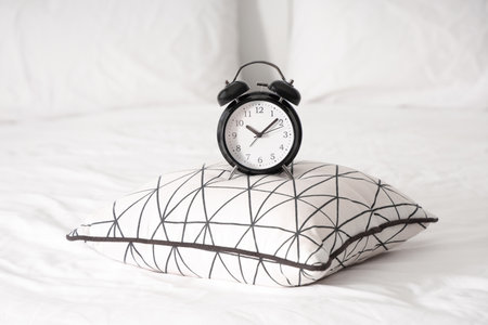 Alarm clock and pillow on bed in bedroom, closeupの写真素材