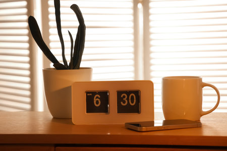 Alarm clock, houseplant, mug of tea and mobile phone on table in dark living room, closeupの写真素材