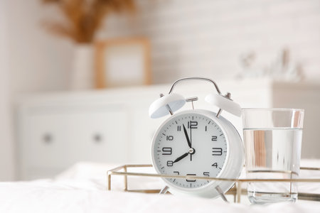 Tray with alarm clock and glass of water on bed in bedroom, closeupの写真素材
