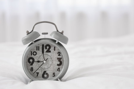 Gray alarm clock on bed in light bedroom, closeupの写真素材