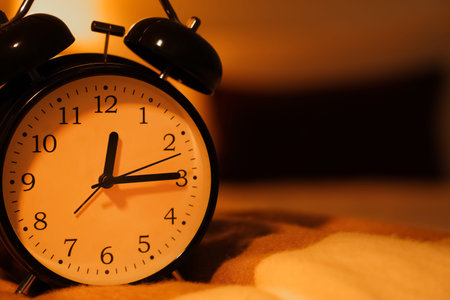 Black alarm clock on bed in dark bedroom, closeup
