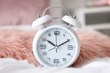 Alarm clock on bed in light bedroom, closeup