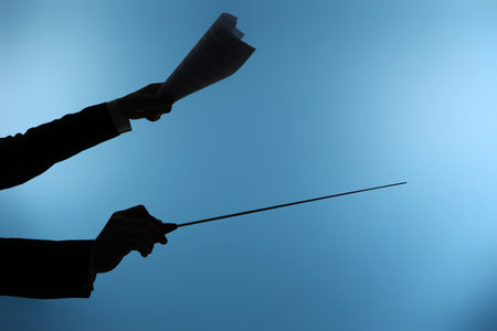 Silhouette of male conductor's hands with baton and note sheet on blue backgroundの写真素材