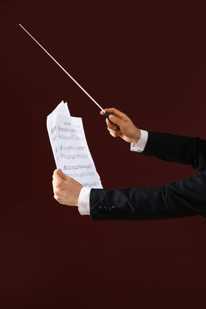 Hands of male conductor with baton and note sheet on brown background