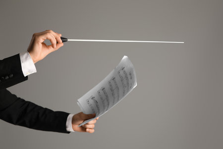 Hands of male conductor with baton and note sheet on gray backgroundの写真素材