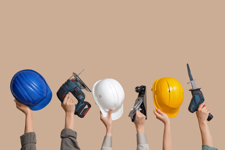 Hands with hardhats and construction tools on beige backgroundの写真素材