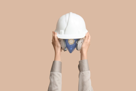 Hands with hardhat and respirator mask on beige backgroundの写真素材