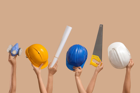 Hands with hardhats and construction tools on beige backgroundの写真素材