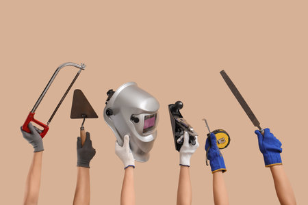 Hands with welding mask and construction tools on beige backgroundの写真素材