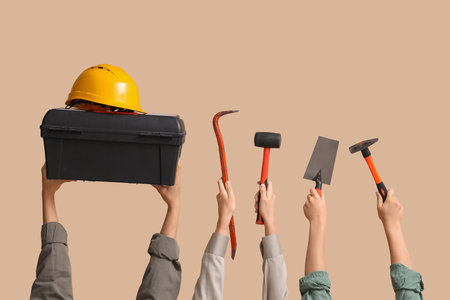 Hands with hardhat, tool box and construction tools on beige backgroundの写真素材